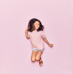 Adorable hispanic child girl wearing casual clothes smiling happy. Jumping with smile on face over isolated pink background