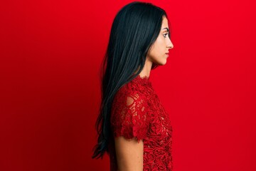 Beautiful hispanic woman wearing elegant clothes over red background looking to side, relax profile pose with natural face with confident smile.
