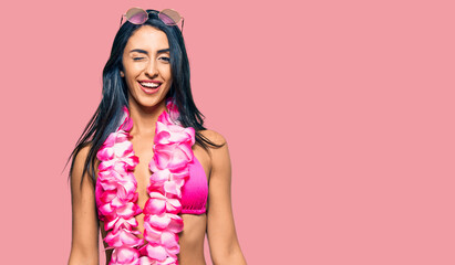 Beautiful hispanic woman wearing bikini and hawaiian lei winking looking at the camera with sexy...