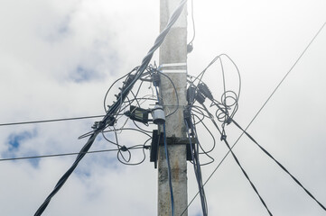 An old power pole with a bunch of tangled power grids against a cloudy sky