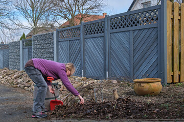 Seasonal garden work. Woman cleaning a path way to a detached house