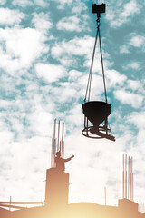 Silhouette of builder on the top of an unfinished construction with with a suspension of a concrete mixer on a crane against the blue sky with clouds.