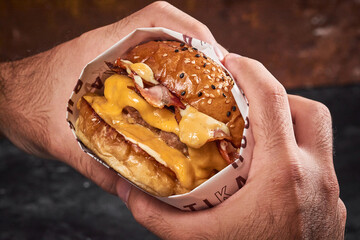 manos cogiendo hamburguesa doble carne con tocineta queso derretido y cebolla en un fondo rustico