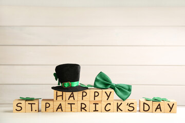 Leprechaun hat, green bow tie and wooden cubes with words Happy St Patrick's Day on white table,...