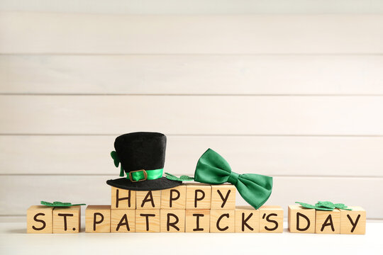 Leprechaun hat, green bow tie and wooden cubes with words Happy St Patrick's Day on white table, space for text