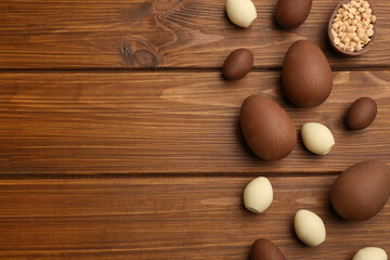 Sweet chocolate eggs and candies on wooden table, flat lay. Space for text