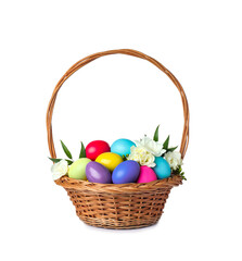 Wicker basket with bright painted Easter eggs and spring flowers on white background