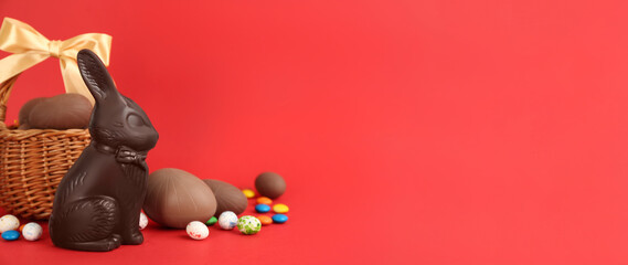 Chocolate Easter bunny, eggs and candies on red background. Space for text