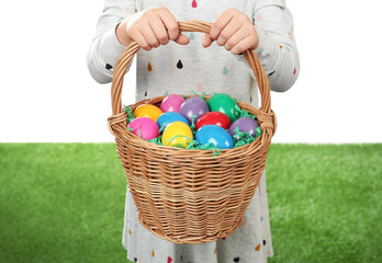 Little girl with basket full of Easter eggs on green grass against white background, closeup © New Africa