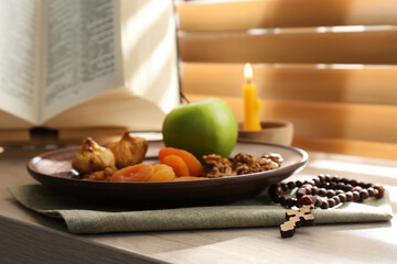 Dried fruits, apple, prayer beads, Bible and candle on window sill indoors. Great Lent season