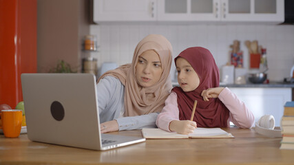 A young mother with a turban is helping her little daughter who is receiving distance education...