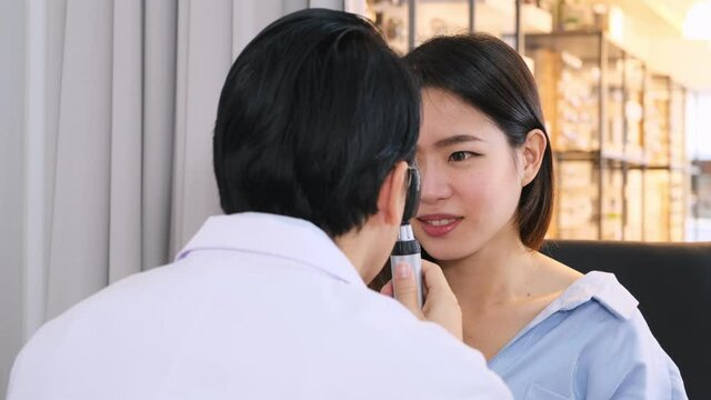 Ophthalmologist using ophthalmoscope to look into eyes of cute woman patient. 