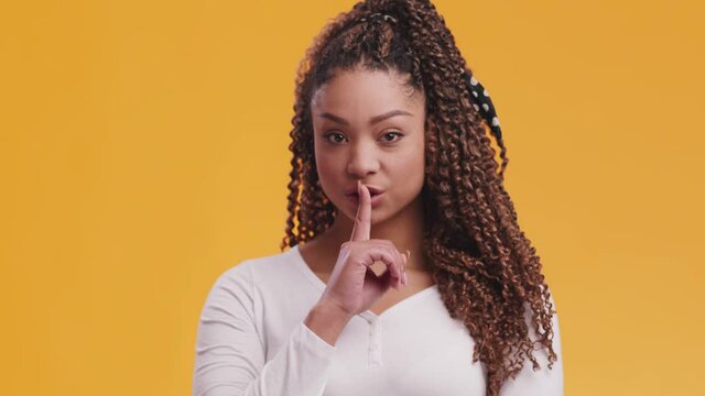 Hush. Studio portrait of young african american showing secret gesture, putting finger on lips, orange background