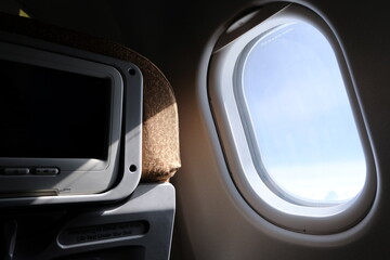 Airplane window with inflight entertainment shining by sun