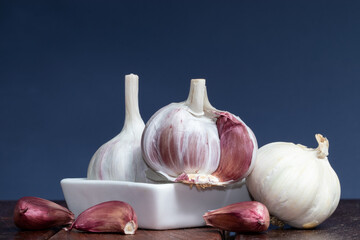 Garlics in a white bowl on .wooden table and blue background.