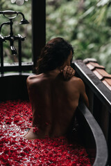 Woman relaxing in round outdoor bath with tropical flowers, organic skin care, luxury spa hotel,