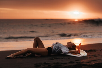 Fototapeta na wymiar Beautifull woman on tropical beach holding surfboard at sunset in Bali
