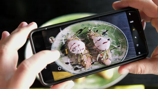 A woman in a restaurant takes a picture of food with a mobile phone camera. Sandwich with poached egg and avocado and salmon