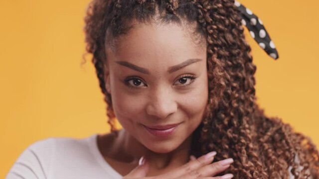 Close up portrait of young grateful african american woman touching her chest with gratitude, orange background
