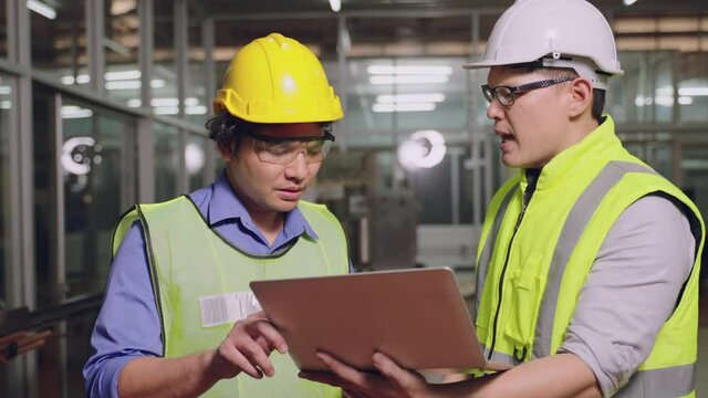 Asian manager feeling upset with the engine machine of the factory arguing about planning procedure of work, he scolding industrial workers for low level of quality standing in factory workshop