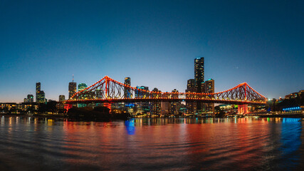 Naklejka premium Panorama night view of buildings and bridge with nice reflection by the port during twilight blue hour in Brisbane, Queensland, Australia