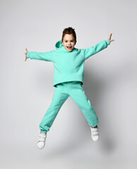 Fototapeta na wymiar Active positive kid boy in stylish casual sport suit green, mint color hoodie and pants is jumping high, flying over white background