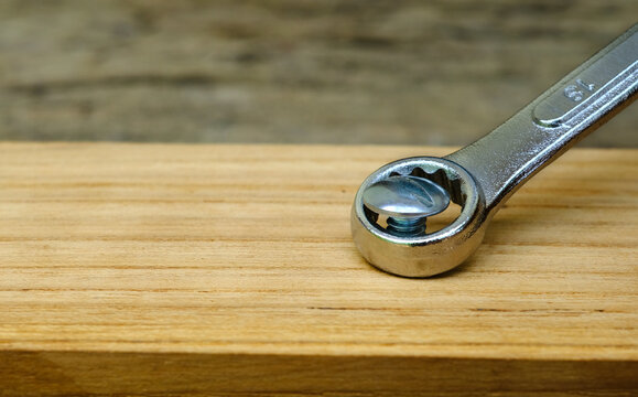 Close-up wrench screwing nut a furniture screw into a wooden plank, The effort  wrong of tools as a fail concept