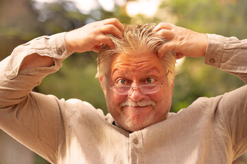 A man with glasses keeps his hands on his head and thinks hard.
