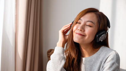 A beautiful young asian woman enjoy listening to music with headphone at home