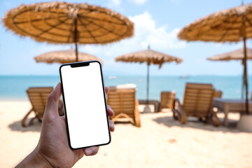 Mockup image of a man holding mobile phone with blank desktop screen while sitting on the beach