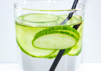 Detox water with a sliced cucumber in a glass with a straw for drinking. The concept of losing weight and cleansing the body. Macro.