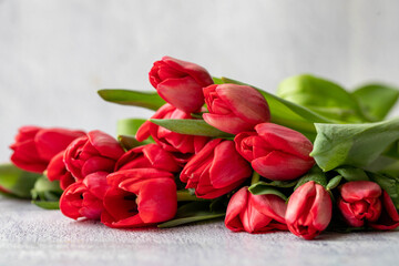 Bouquet of many bright red tulips lies on a light grey concrete background. side view, horizontal