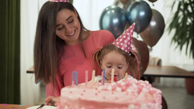 Mom and daughter are sitting at home at the table and celebrating their birthday. The girl is holding a red box in her hands.