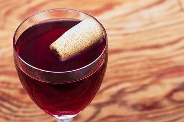 a glass of dry red wine on a wooden table with a cork floating in the glass