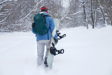 Snowboarder guy carries a board while climbing the mountain. He is wearing a jacket, hat and ski mask. Pull up during freeride