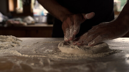 Obraz na płótnie Canvas Male chef kneading homemade dough on wooden table