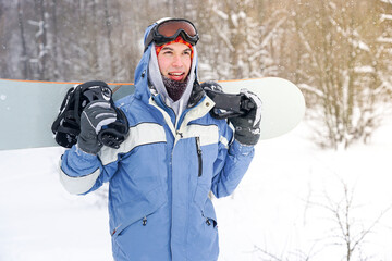 Guy snowboarder carries a snowboard. He holds the snowboard in his hands and walks along the snowy...