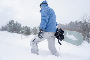 The guy snowboarding goes on a snowy slope. He is holding a snowboard