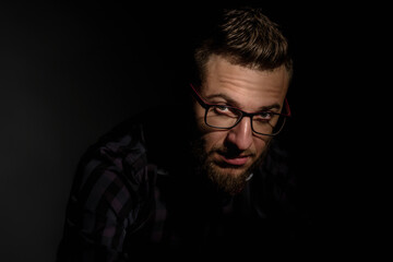 Studio portrait of young bearded man in glasses on dark background