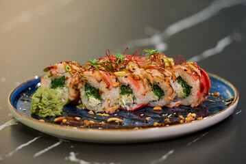 Sushi rolls with Chuka wakame seaweed, Philadelphia cheese, and shrimps on a blue ceramic plate with sauce, peanuts, ginger, and wasabi on a black stone table.