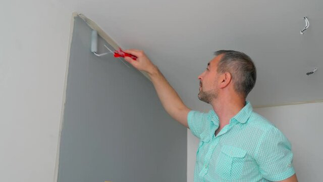 A man in a shirt Paints the walls with a roller gray. Repair of the premises.