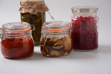 Jars of Homemade pickled vegetables: cucumbers, tomatoes, honey agarics mushrooms, on white  background. Marinated and Fermented food. Fermented preserved vegetarian food concept.
