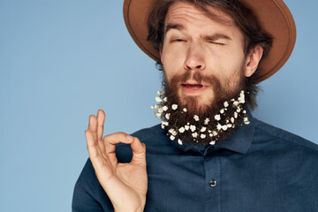 Cute man in a hat flowers in a beard emotions close-up blue background