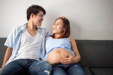 Portrait of beautiful asian pregnant woman and her husband on the sofa in house.