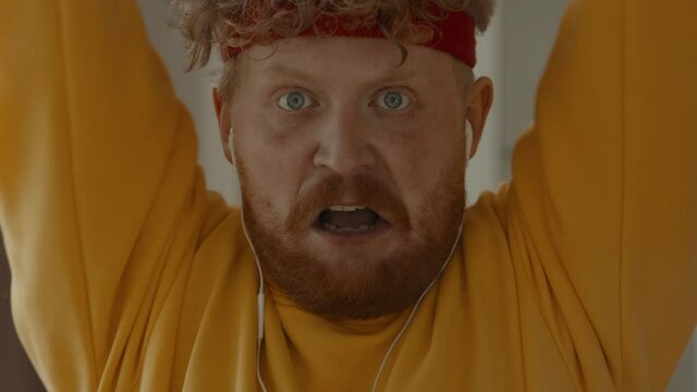 CARSH ZOOM Portrait of funny overweight Caucasian man working out with dumbbells at home, looking into camera. Bright, commercial high key advertising style lighting