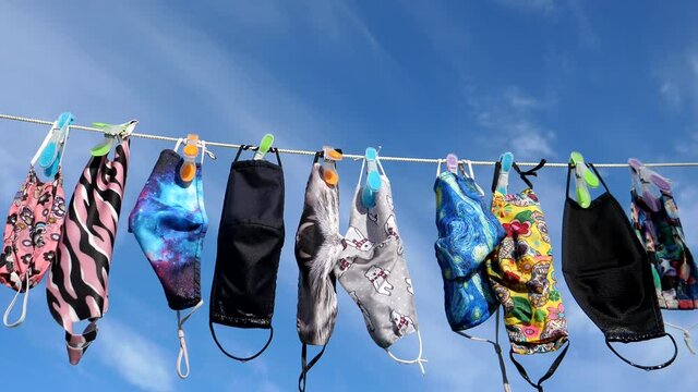 Reusable laundered protective face masks drying on clothesline against blue sky.