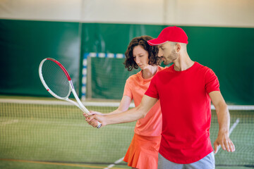 Man in a red cap and with a racket having a workout with his female coach