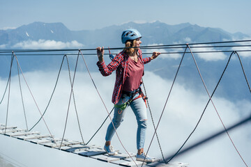 A happy woman walks on a suspension bridge high in the mountains at the level of a cloud. Wanderlust and adventures. Extreme vacation.