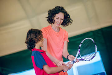 Woman in bright clothes teaching a boy to hold a tennis racket