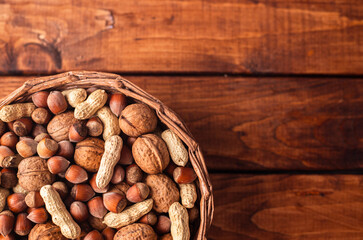 nuts lie in a wicker basket on a wooden table. peanuts, hazelnut, and walnut nuts mixed on wooden...